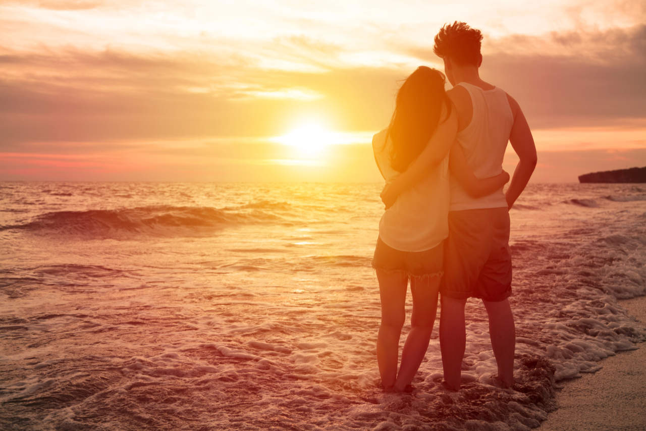 Ein umschlungenes Paar am Strand bei Sonnenuntergang.