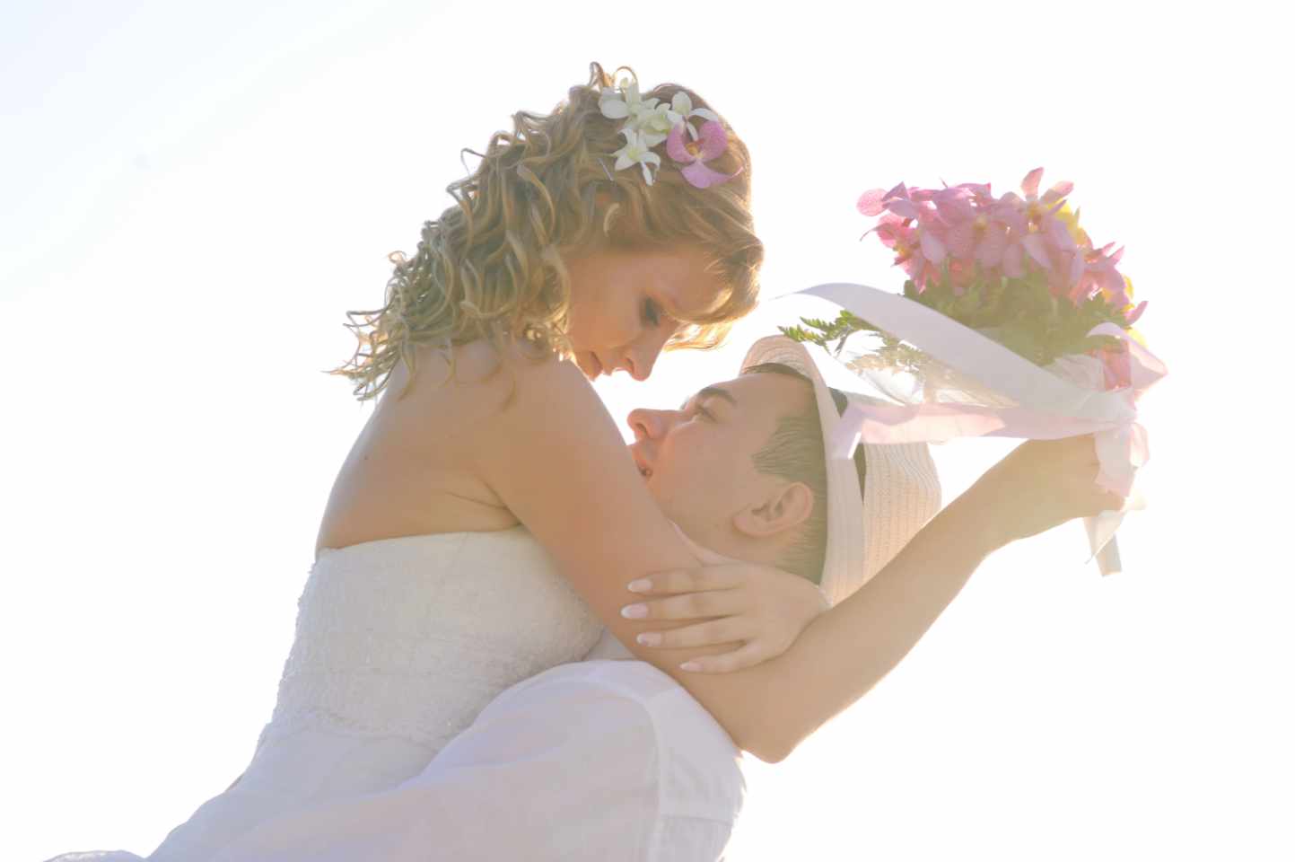 Ein Brautpaar, er hebt sie hoch, sie hat einen Bluemstrauß in der Hand, sie schauen sich an