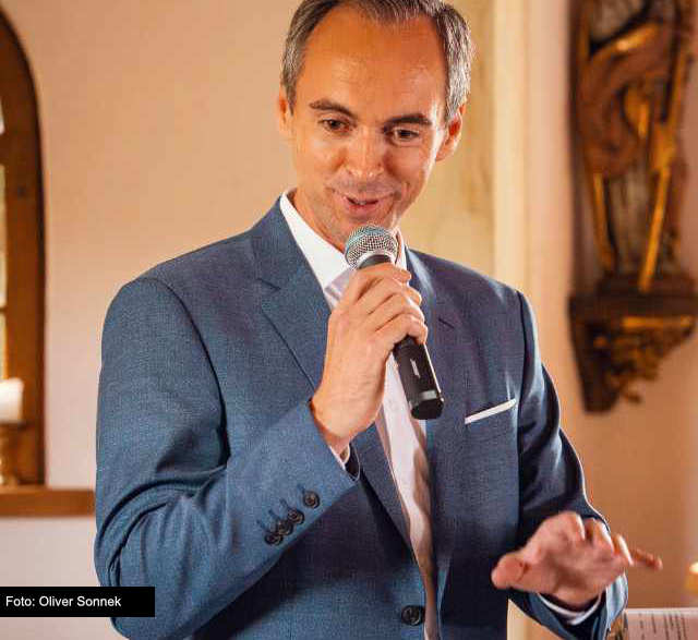 Oliver Metzger, Freier Trauredner, Hochzeitsredner, Trauerredner und Kinderwillkommensredner, mit Mikrofon in der Hand bei einer freien Trauung in einer Kirche auf dem Sonnenhof in Aspach in der Nähe von Ludwigsburg zwischen Heilbronn und Stuttgart - Freie Trauung, Hochzeit, Trauredner finden, Hochzeitsredner 